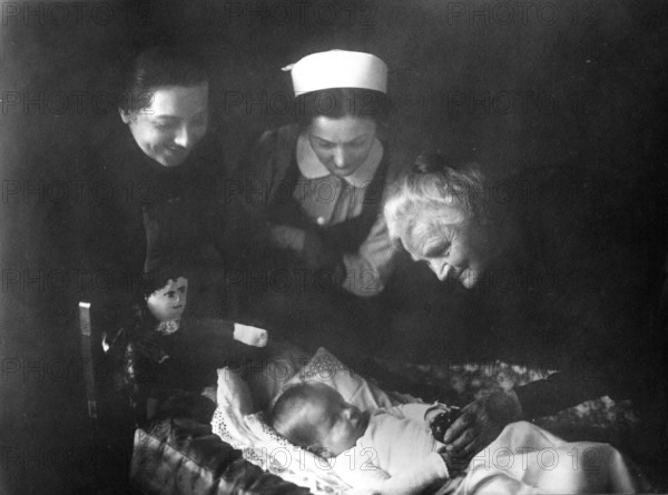 Women and baby, 20s, 1920s, Three woman gently looking at a sleeping baby in a dim light, Historical photograph