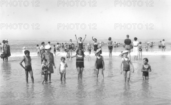 Children in the water, 1920s, Children playing in shallow water on the beach under a clear sky. A cheerful summer scene, historical photo