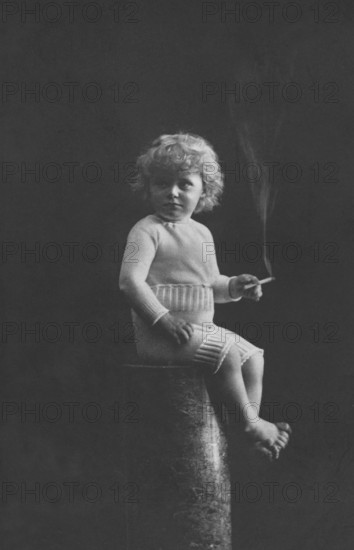 Child smoking, 1920s, A child in historical clothing sits on a pedestal and holds a cigarette in his hand, Historical photo