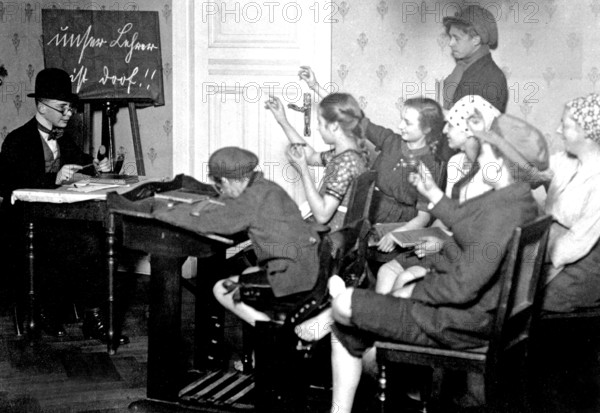 Young people playing school, ca. 1920, children in the classroom writing with pencils while the teacher explains on the blackboard, historical photo