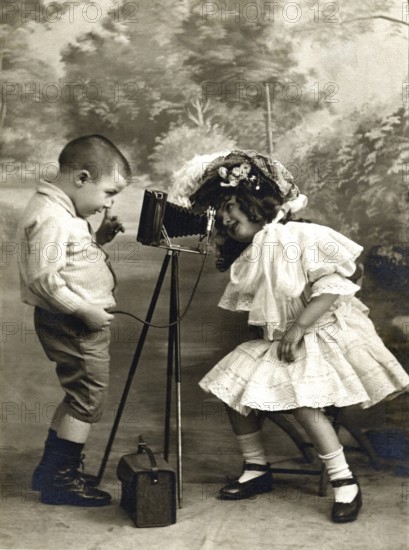 Children's camera self-timer 1906, Two children playing with an old camera, one looking at the lens, Historical photo