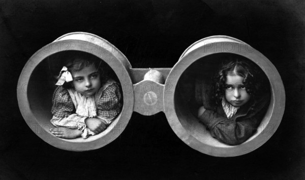 Two girls in binoculars, 1920s, Two children looking through oversized binoculars in a black and white portrait, Historical photo