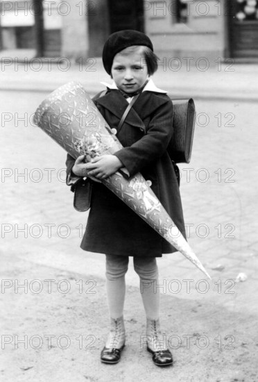 Little girl with school cone, 1940, A child in school uniform holding a large sugar cone on the street, historical photo