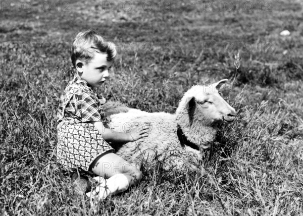 Little boy and lamb in the grass, 1930s, A boy sits lovingly next to a sheep in a meadow, Historical photo