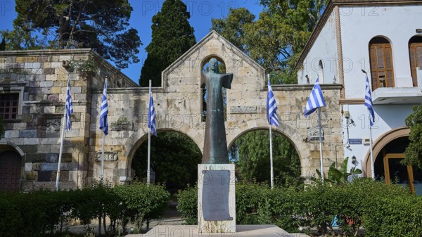 Statue surrounded by Greek flags and historical architecture in the garden, Kos Town, Venetian City Gate, Castle, Kos, Dodecanese, Greek Islands, Greece