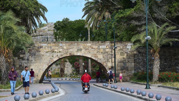 Street scene with arched bridge and people under palm trees along the road, Bridge, Neratzia Castle, Kos Town, Kos, Dodecanese, Greek Islands, Greece
