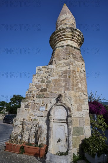 Historic fountain next to a stone tower under a clear blue sky, Eski Cami, Minaret, Kos Town, Kos, Dodecanese, Greek Islands, Greece