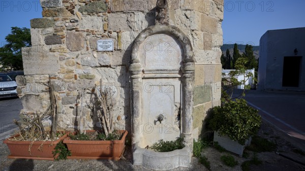 Small stone fountain by an old wall, surrounded by plants under a blue sky, Minaret, Eski Cami, Kos Town, Kos, Dodecanese, Greek Islands, Greece