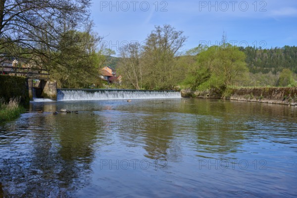 Calm river water in front of a dam wall, surrounded by green nature and blue sky, spring, Obersinn, Sinntal, Spessart, Bavaria, Germany