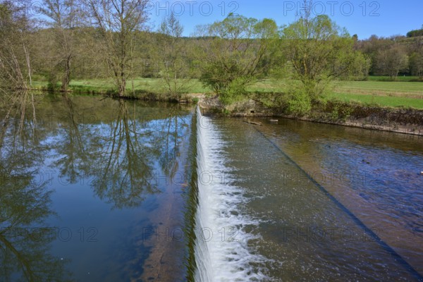 Small dam wall with falling water and reflection of the trees in the river, spring, Obersinn, Sinntal, Spessart, Bavaria, Germany