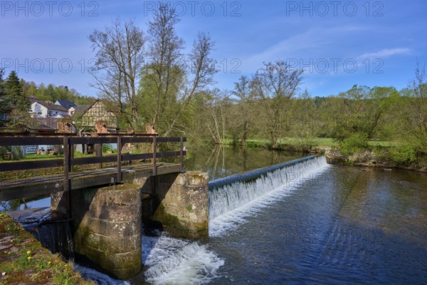 A weir bridges a river, surrounded by fresh green trees, spring, Obersinn, Sinntal, Spessart, Bavaria, Germany