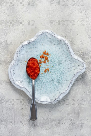 A spoon with orange flying fish caviar, Tobiko, on a light blue plate, caviar for rolls and sushi, close-up