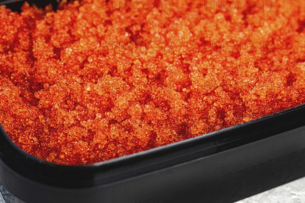Container with orange caviar, flying fish, Tobiko, on the table, caviar for rolls and sushi, close-up