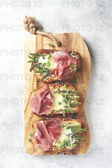 Open sandwiches with asparagus and prosciutto, with cheese, breakfast, on a wooden serving board