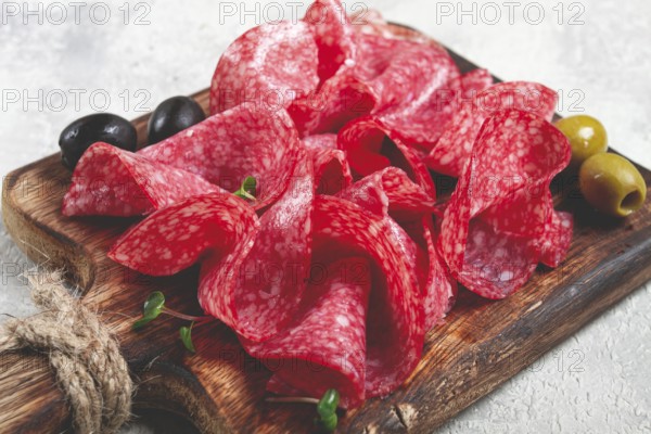 Sliced salami sausage, on a wooden chopping board, decorated with olives and herbs, close-up, no people