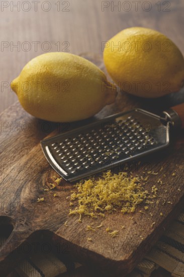 Lemons and grated orange peel, with a zest grater, on a chopping board, close-up, no people