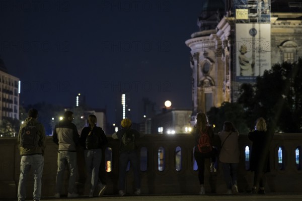 People watching the rising moon from the Friedrichsbrücke bridge next to Berlin Cathedral, Berlin, 11 June 2025