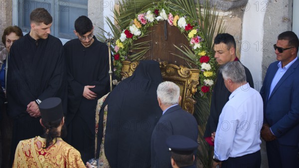 A priest prays in front of a wreath decorated with flowers, surrounded by people in traditional and modern dress, Orthodox ceremony, monks of St John's Monastery, ceremonial washing of feet, procession, Maundy Thursday, Megali Pempti, Chora, Patmos, Dodecanese, Greek Islands, Greece