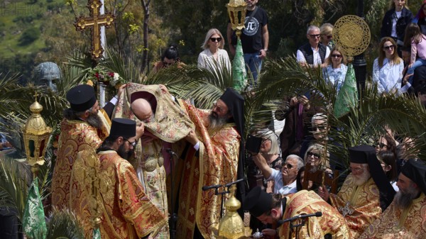 Priests standing under a cross during an outdoor religious ceremony surrounded by worshippers and palm trees, Orthodox ceremony, monks of St John's Monastery, ceremonial washing of feet, procession, Maundy Thursday, Megali Pempti, Chora, Patmos, Dodecanese, Greek Islands, Greece