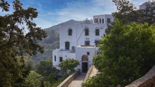 White monastery building surrounded by dense vegetation and a sunny sky, Monastery of the Revelation, Moni tis Apokalipsis, World Heritage Site 1999, Patmos, Dodecanese, Greek Islands, Greece