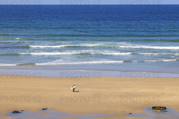 Man with a surfboard walking on a sand beach by the sea a sunny summer day, Crozon peninsula, Bretagne, France
