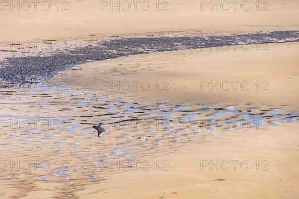 Man with a surfboard walking on a sand beach on the way to the sea a sunny summer day, Crozon peninsula, Bretagne, France