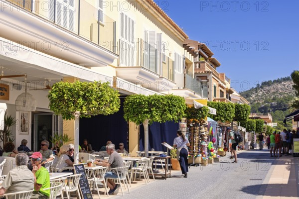 Outdoors restaurant on a street with tourist sitting in the sunshine in an idyllic village, Sant Elm, Mallorca, Spain