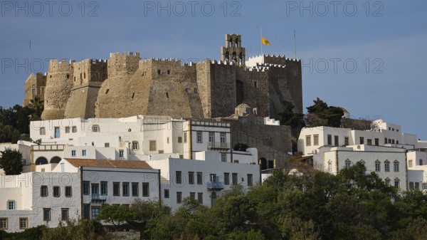 Historic castle on hill with white buildings in the foreground and flag in the sky, Monastery of St John the Theologian, Monastery of St John the Theologian, World Heritage Site 1999, main entrance, Chora, Patmos, Dodecanese, Greek Islands, Greece