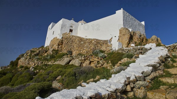 White building with stone steps and vegetation on rocky terrain under a blue sky, Church of the Prophet Elias, Profitis Ilias Chapel, Hermitage, Patmos, Dodecanese, Greek Islands, Greece