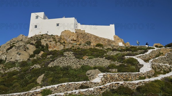 White buildings on a hill with stony paths and abundant vegetation, Church of the Prophet Elias, Profitis Ilias Chapel, Hermitage, Patmos, Dodecanese, Greek Islands, Greece