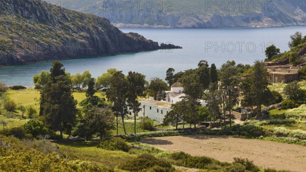 Small village on a rocky coast, surrounded by trees and blue sea, Limoni Kalogiron Monastery, Livadi Kalogiron, Patmos, Dodecanese, Greek Islands, Greece