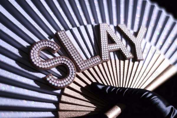 Close-up of drag queen's rhinestone SLAY fan held in black satin glove with glitter and warm lighting. Generative AI, AI generated