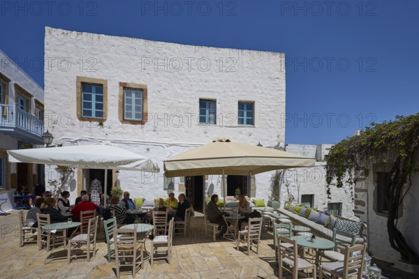People sitting at tables under parasols on a sunny café terrace, Platia Lesvias, Chora, UNESCO World Heritage Site 1999, Patmos, Dodecanese, Greek Islands, Greece