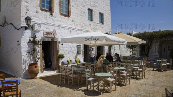 Cosy café terrace with parasols and rustic white buildings in the background, Platia Lesvias, Chora, UNESCO World Heritage Site 1999, Patmos, Dodecanese, Greek Islands, Greece