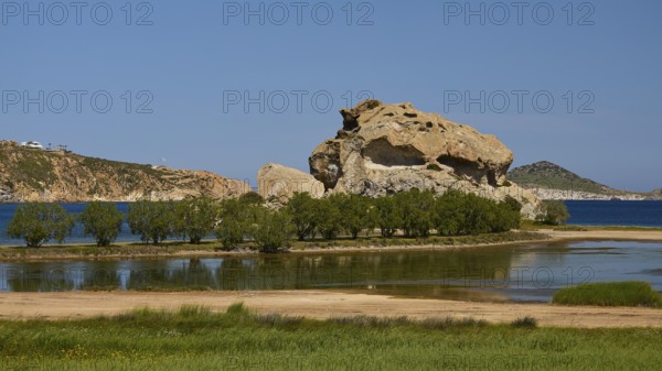 Massive rock formation surrounded by water and trees under a clear sky, seasonal salt lake, Grikos, rocks of Kalikatsou, Patmos, Dodecanese, Greek Islands, Greece