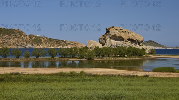 Rock in a lush green landscape with water and trees under a sunny sky, Rock of Kalikatsou, Seasonal Salt Lake, Grikos, Patmos, Dodecanese, Greek Islands, Greece
