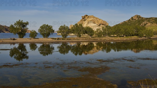 Rocks and trees reflected in a calm lake under a clear sky, Rocks of Kalikatsou, Seasonal Salt Lake, Grikos, Patmos, Dodecanese, Greek Islands, Greece