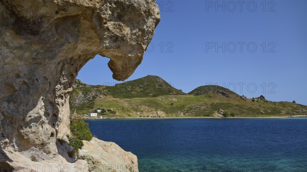 Large rock overlooking the clear blue sea with green hills in the background, Tragonisi Island, Rock of Kalikatsou, Patmos, Dodecanese, Greek Islands, Greece