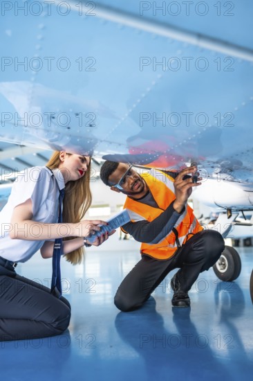 Aircraft maintenance engineer and pilot working together, inspecting the underside of an airplane in a hangar, ensuring safety and compliance