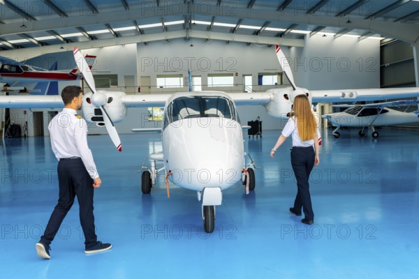 Two pilots walking around a small airplane inside an aircraft hangar, preparing for pre flight checks and ensuring everything is in order