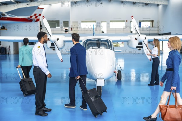 Business people walking towards a private jet with their luggage, accompanied by the pilot and crew in the hangar