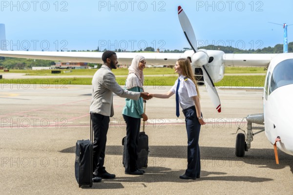 Female pilot greeting two passengers with a handshake next to a private airplane on the tarmac, enjoying a sunny day at the airport