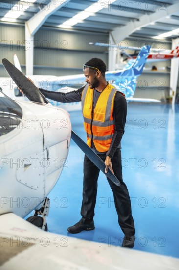 Aircraft maintenance engineer wearing a high visibility vest carefully inspects the propeller of a small airplane inside a hangar
