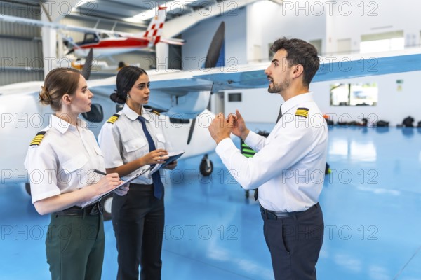 Flight instructor conducting a training session with two pilots inside an aircraft hangar, highlighting aviation education and teamwork
