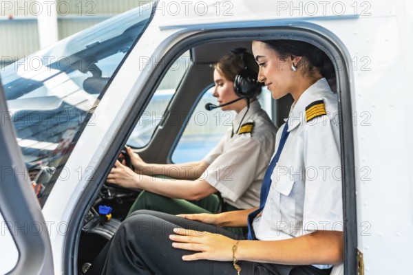 Two female pilots sitting inside the cockpit of a small airplane, preparing for take off, wearing headphones and uniform