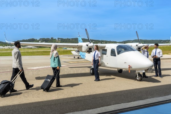 Passengers carrying trolley bags walking towards small airplane and flight crew, ready for boarding on a sunny day at the airport