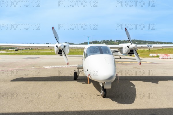 White twin engine turboprop airplane is parked on the tarmac of a small airport on a sunny day, awaiting its next flight