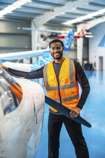 Smiling african american aviation engineer holding a propeller blade, performing maintenance checks in an aircraft hangar
