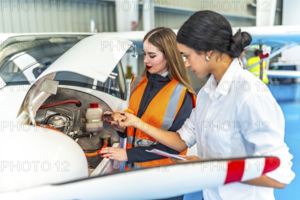Two female engineers in a hangar inspecting an aircraft engine, focusing on maintenance and safety checks, showcasing teamwork and technical expertise