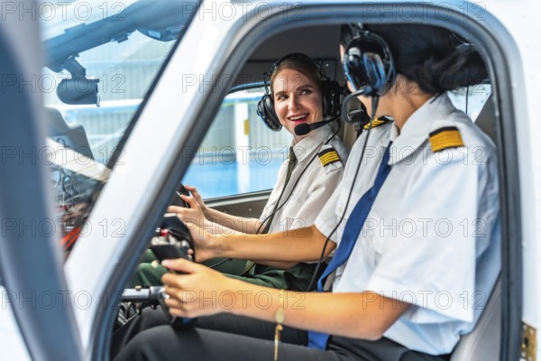 Two smiling female pilots wearing headsets and uniforms are sitting in the cockpit of a small aircraft, operating controls and communicating
